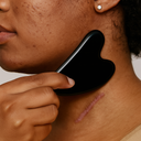 Woman using obsidian gua sha stone for facial scar massage and lymphatic drainage